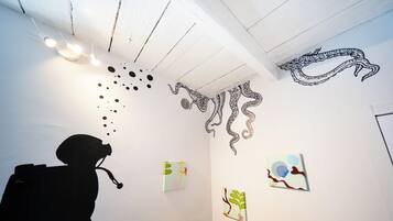 A room with a white ceiling, wall art including a black octopus drawing, and a silhouette of a person.