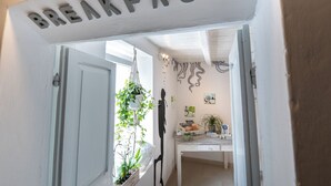 Una puerta con la etiqueta “BREAKFAST” que da a una habitación con un escritorio, plantas y obras de arte en la pared.