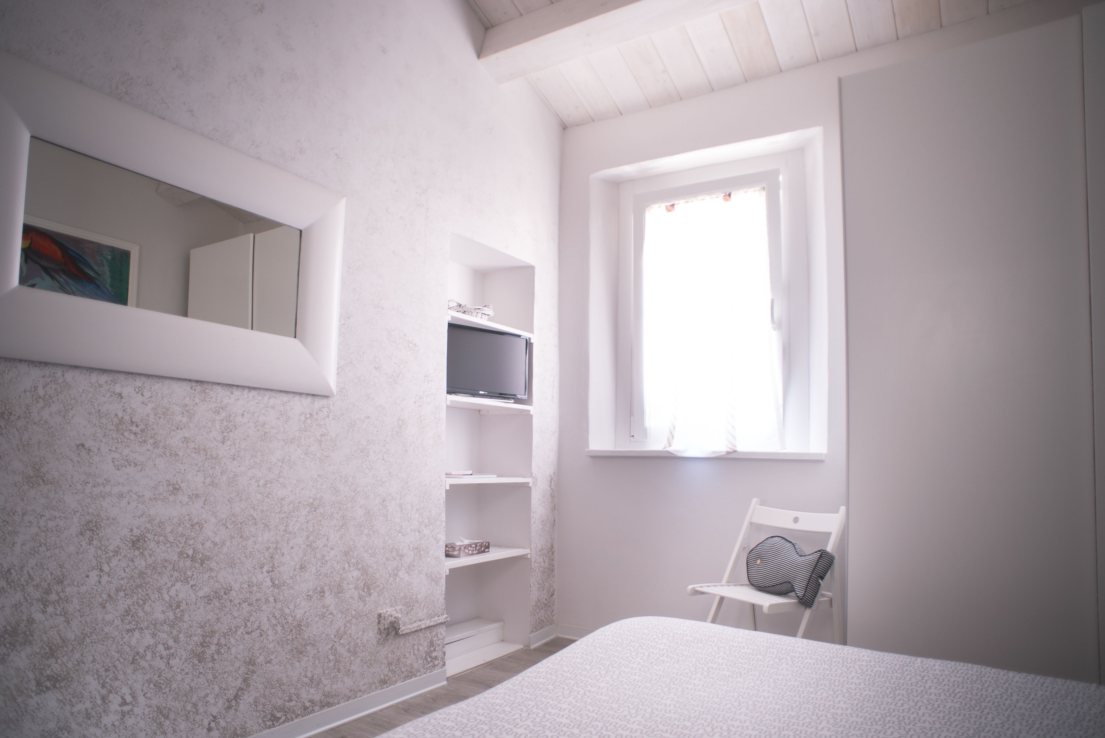 A bedroom with a bed, a chair, a television on a shelf, and a window.