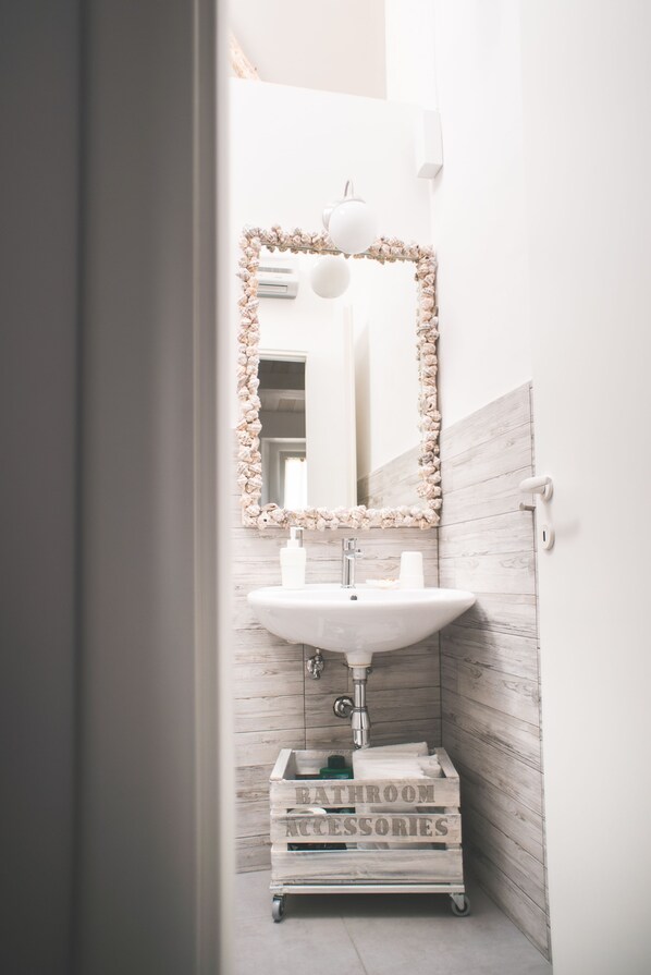 Un baño con lavamanos blanco, espejo con marco floral y armario de madera con la etiqueta 'accesorios de baño'.