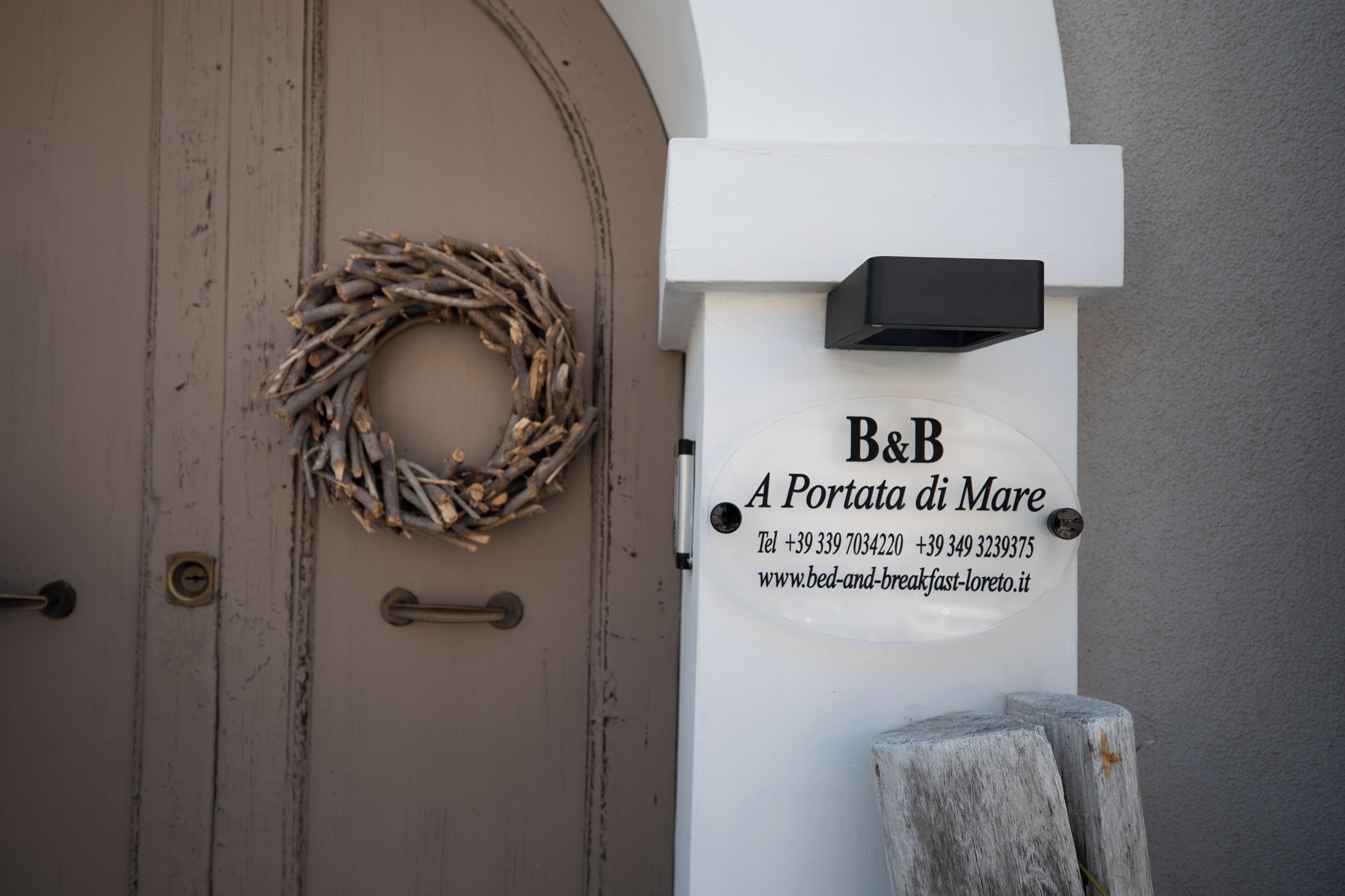 Une porte ornée d’une guirlande et d’une enseigne indiquant le nom « B&B A Portata di Mare », ainsi que les coordonnées.