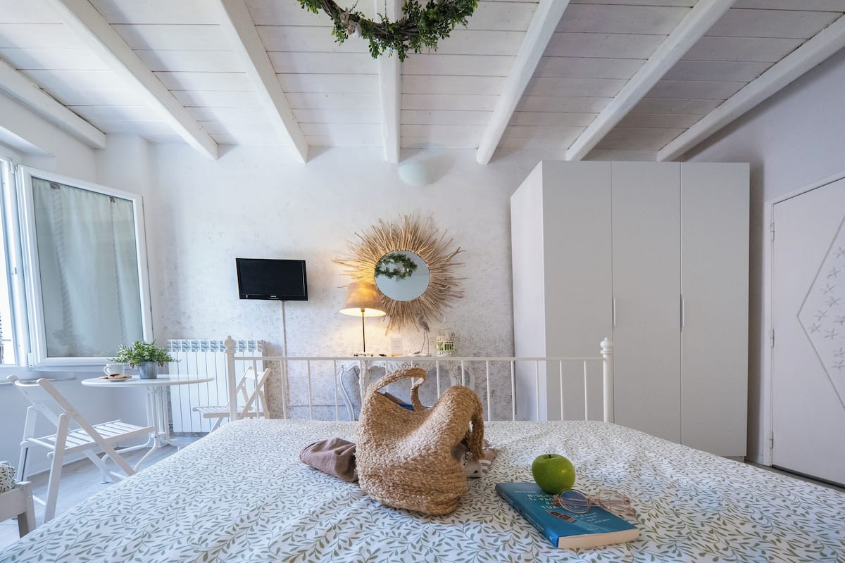 Een gezellige slaapkamer met een bed, een klein tafeltje met een plant, een witte stoel, een televisie aan de muur en een kledingkast.