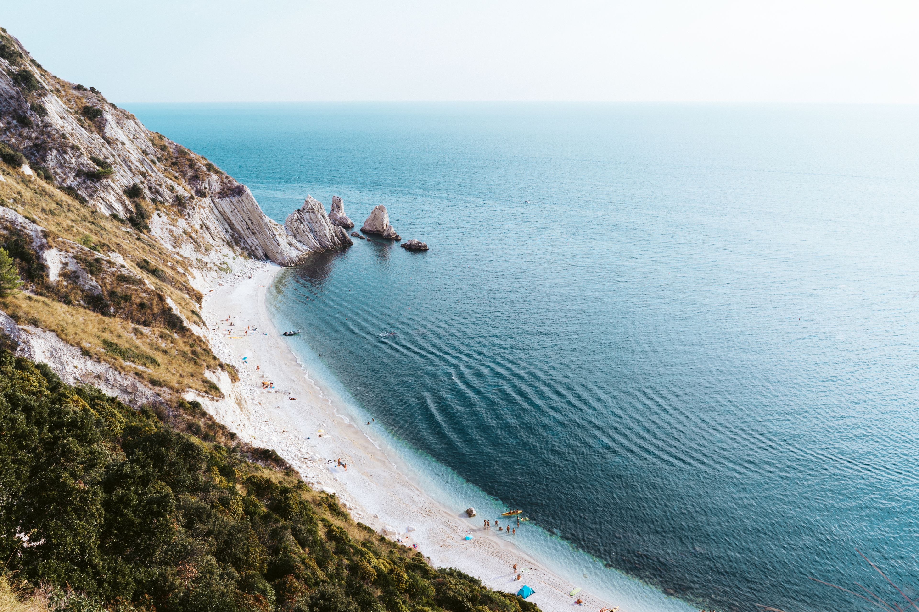 A coastal beach with rocky cliffs and clear blue water.