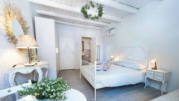 A bedroom with a white bed, bedside tables, a lamp, a mirror, and a potted plant.