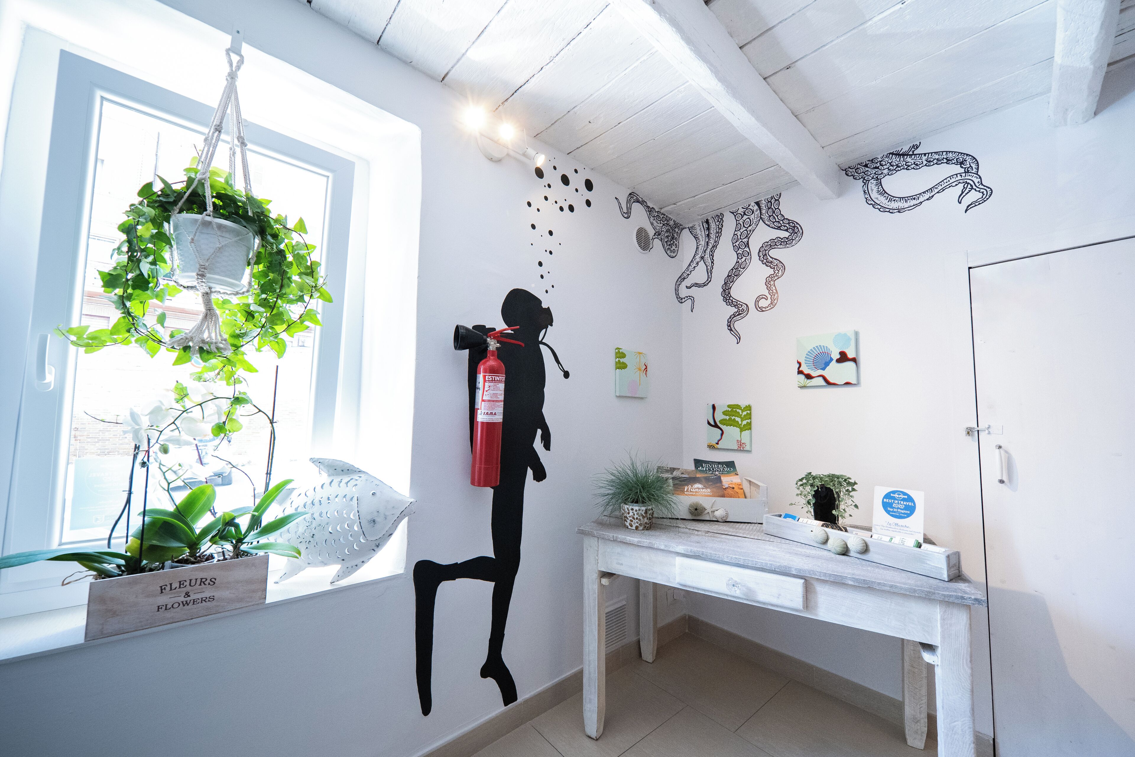 Une pièce avec un bureau blanc, une plante suspendue et des œuvres d’art mural représentant des motifs de poulpes et de poissons.