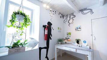 Une pièce avec un bureau blanc, une plante suspendue et des œuvres d’art mural représentant des motifs de poulpes et de poissons.