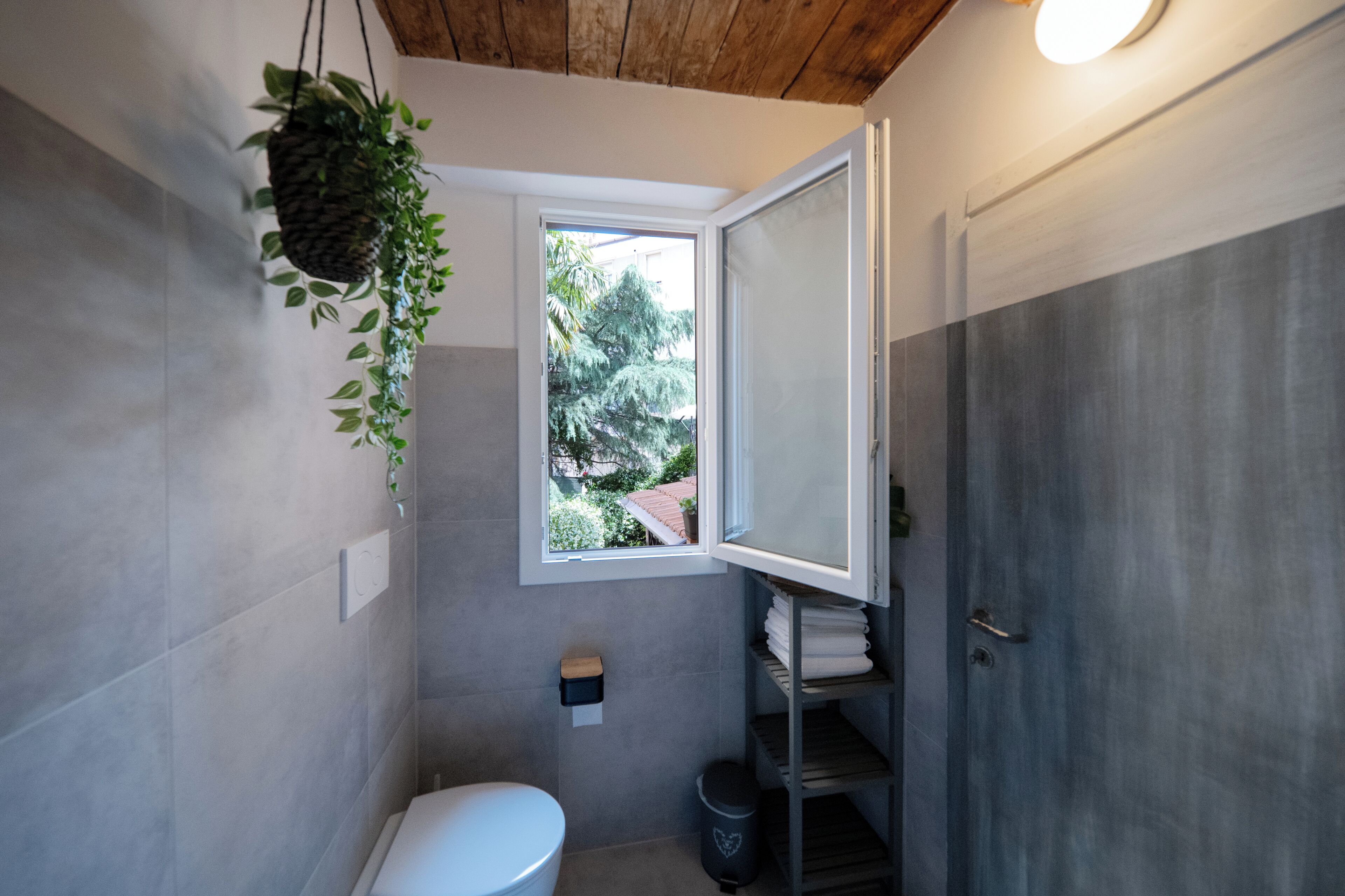 A compact bathroom with a white toilet, a small window, and a wooden ceiling.