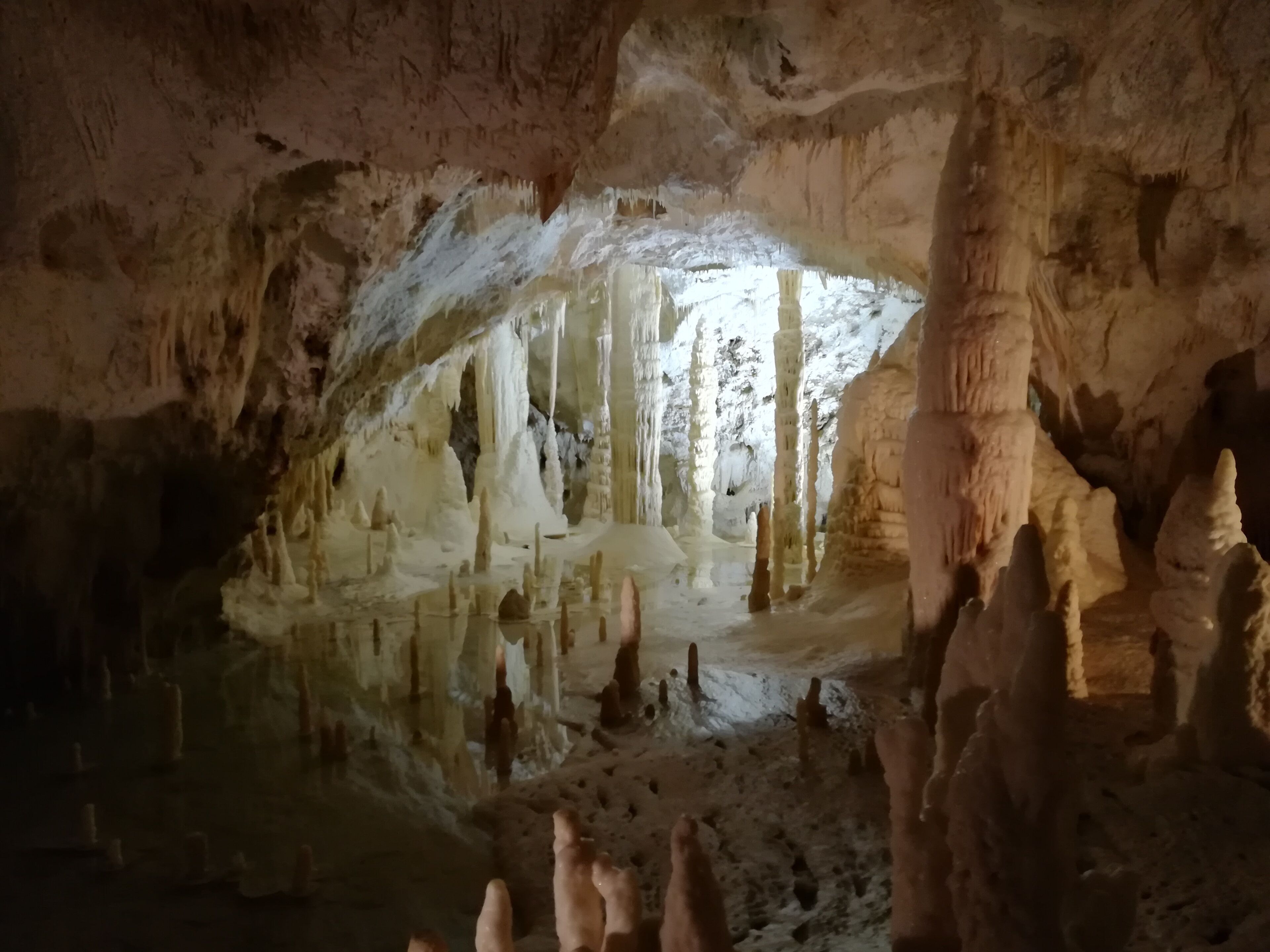 Una cueva subterránea con estalactitas y estalagmitas, un estanque de agua reflectante y un arco natural.