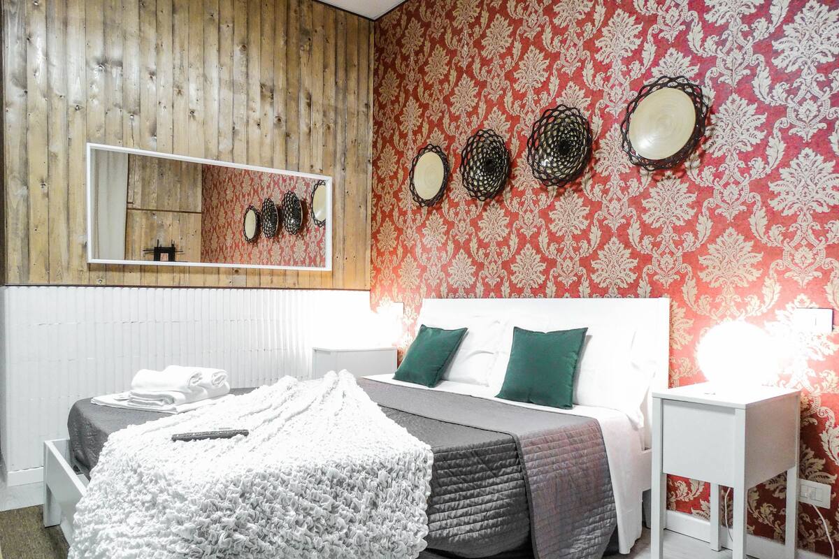 Un dormitorio con cama, mesitas de noche, un espejo y un papel tapiz decorado.