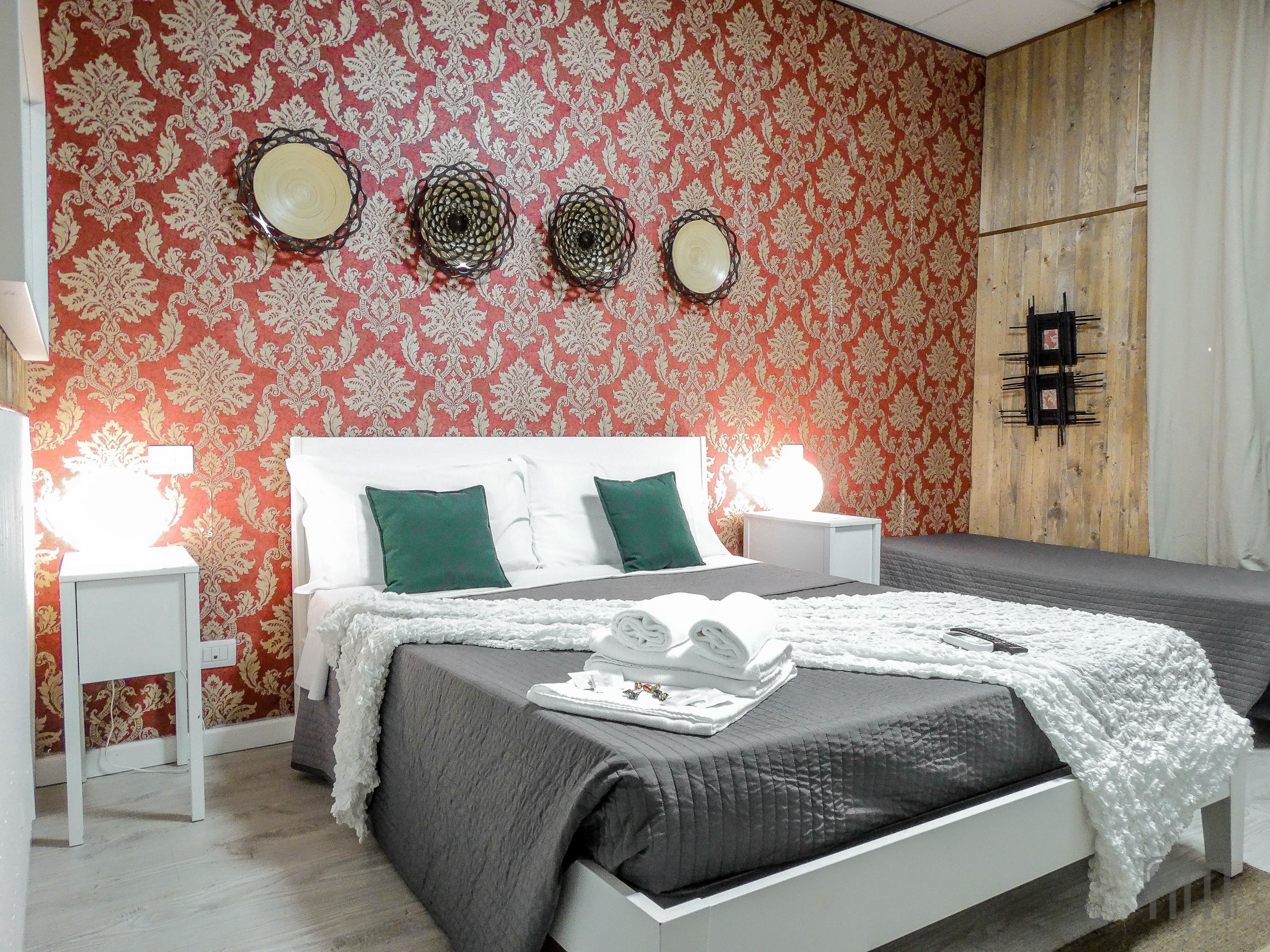 A bedroom with a bed, white nightstands, and a red patterned wall.