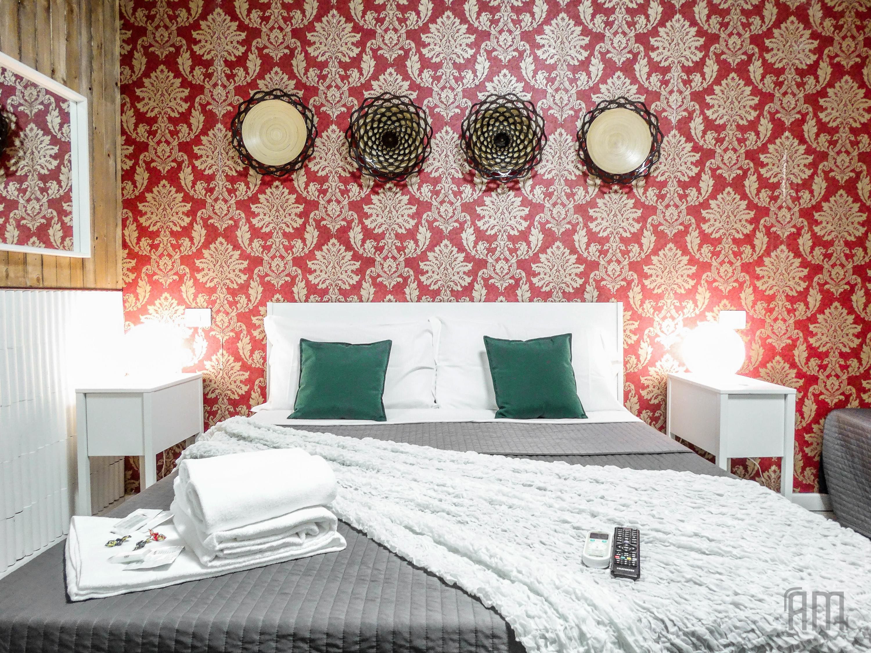 A hotel room with a bed, two pillows, a blanket, a remote control, and a nightstand with a lamp.