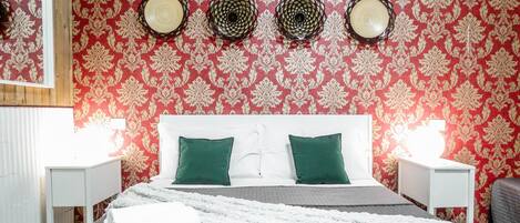 A hotel room with a bed, two pillows, a blanket, a remote control, and a nightstand with a lamp.