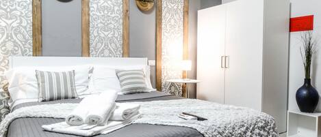 A neatly made bed with pillows and a blanket, a bedside table with a lamp, and a wardrobe.