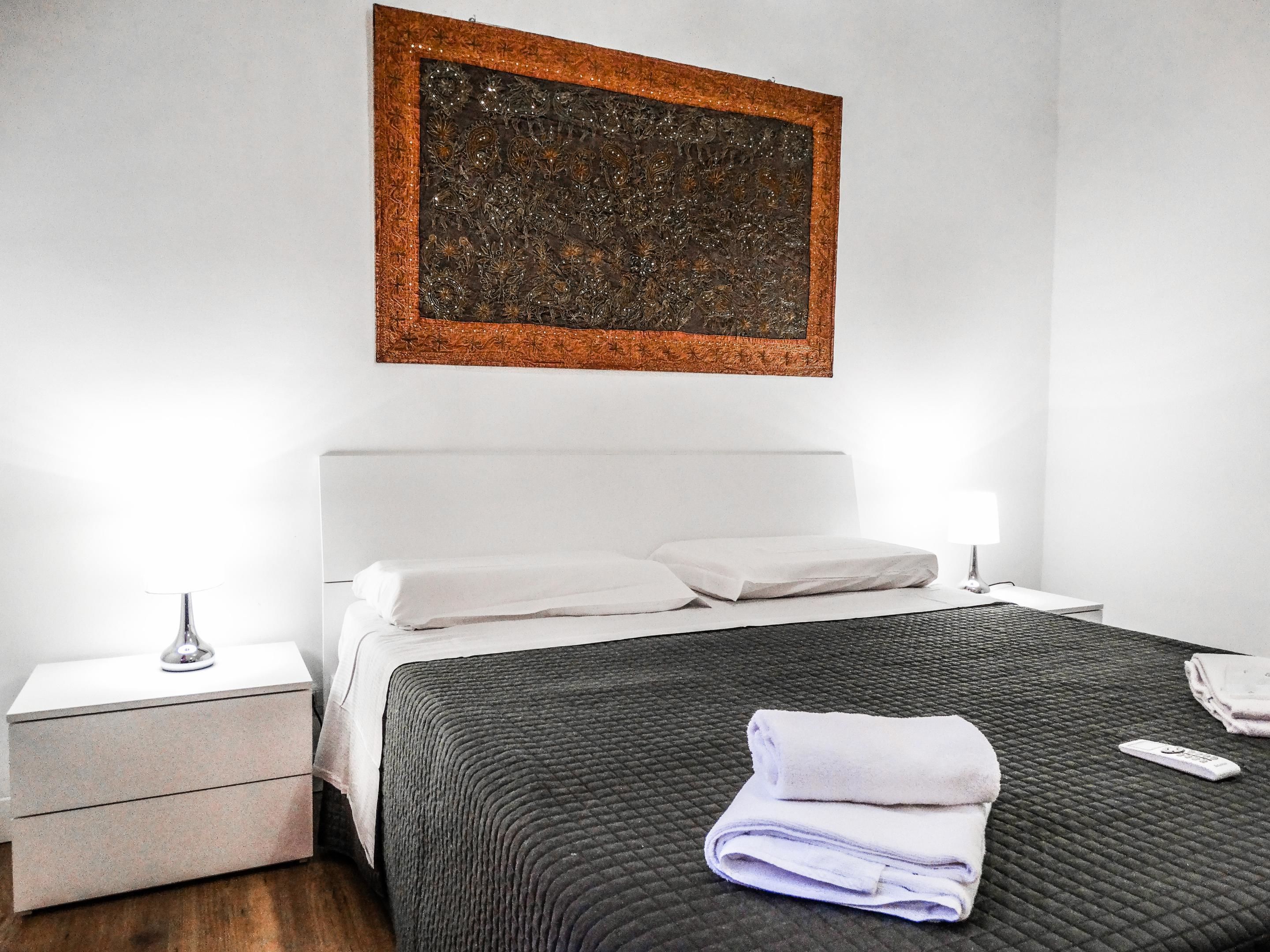 A hotel room with a bed, a nightstand, a lamp, and a painting on the wall.