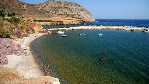 A coastal scene with a rocky shoreline, clear water, and boats anchored near the shore. - Bungalow Musuri (Sitia)