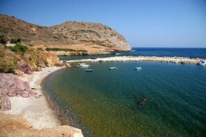 A coastal scene with a rocky shoreline, clear water, and boats anchored near the shore. - Bungalow Musuri (Sitia)