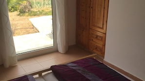 A bedroom with a large window, wooden wardrobe, and a bed with a patterned bedspread. - Bungalow Musuri (Sitia)