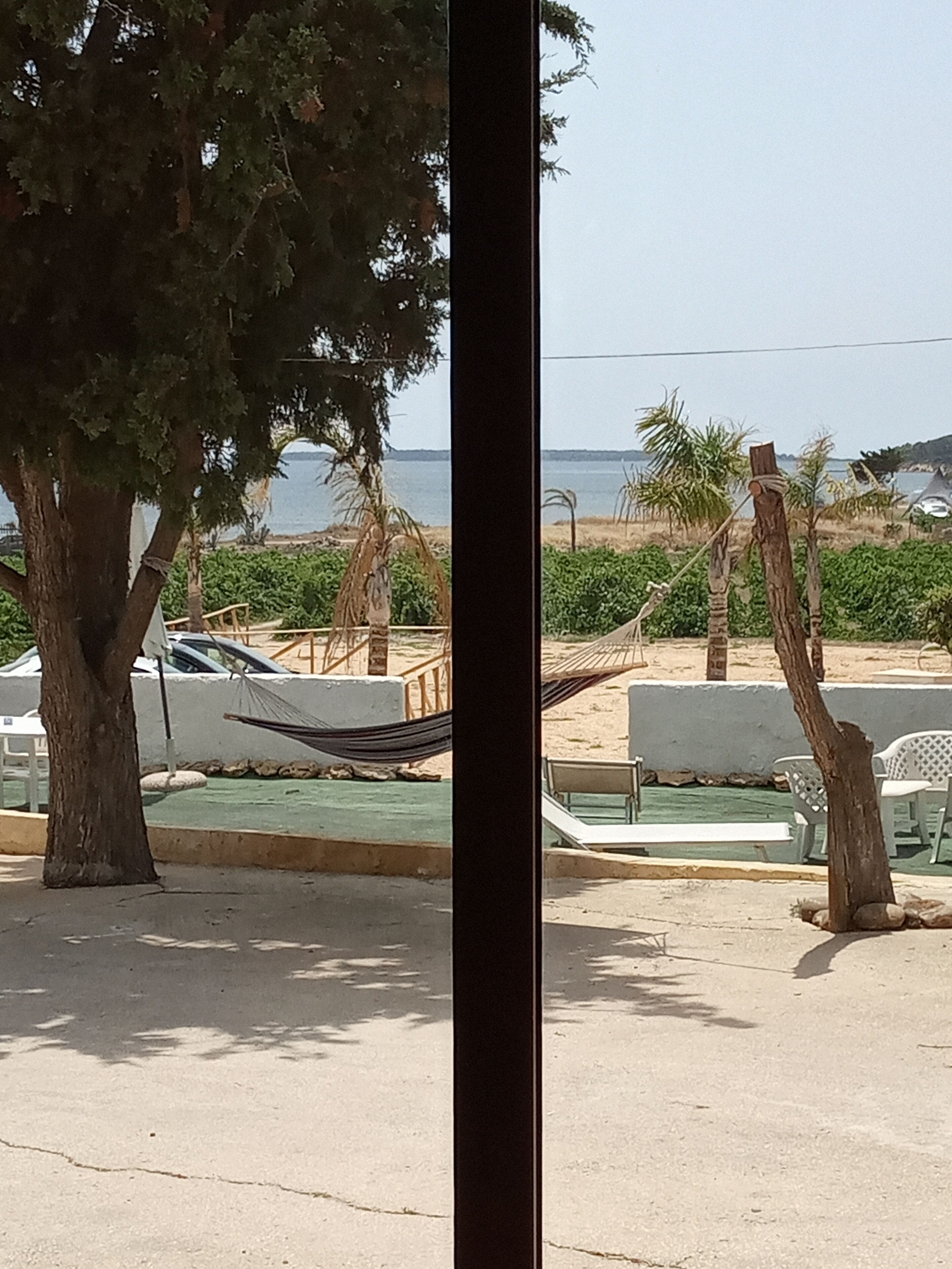 Vista de una zona de playa con una hamaca, sillas y un coche aparcado cerca del agua.