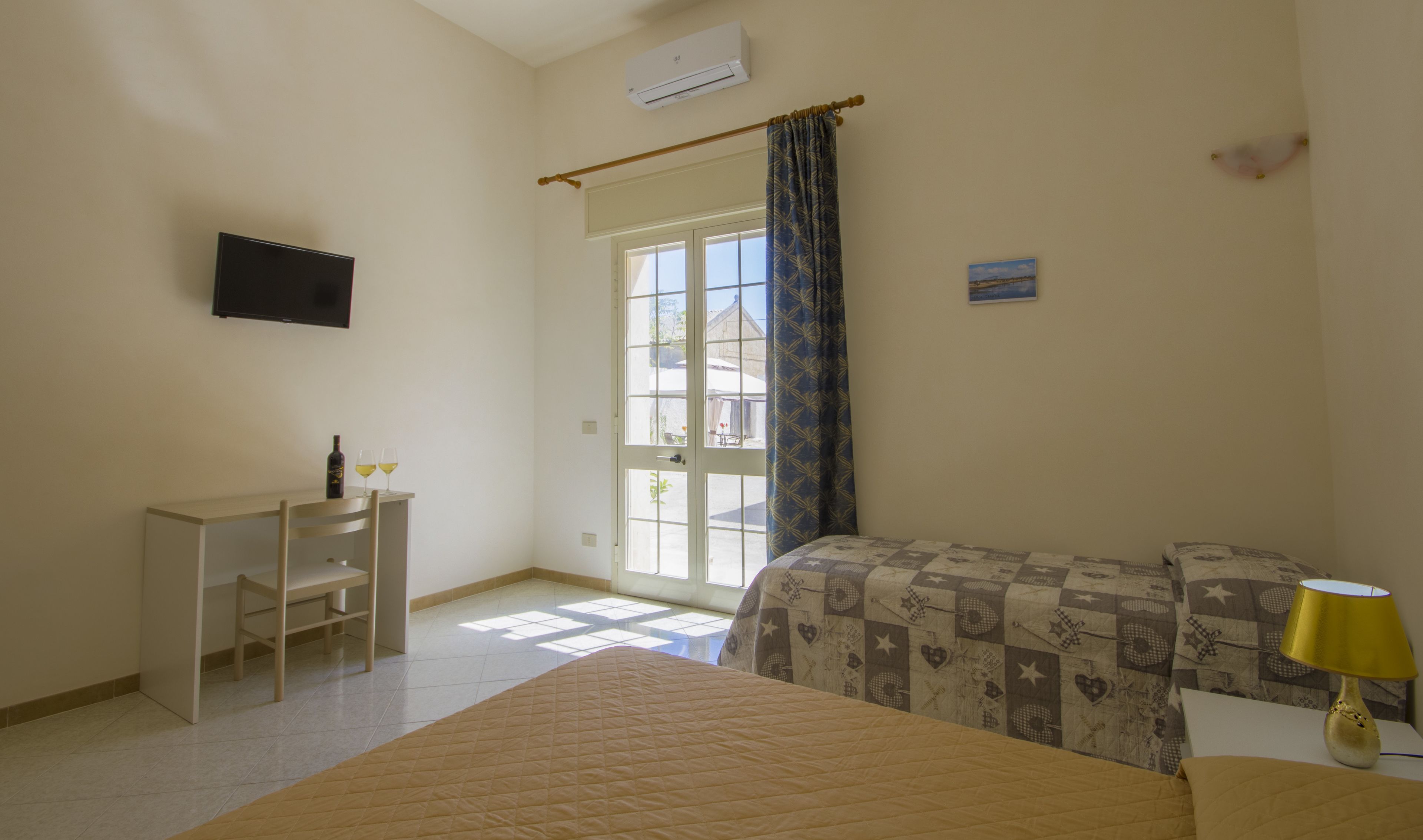 A bedroom with a bed, a desk, a chair, a window with curtains, and a wall-mounted TV.
