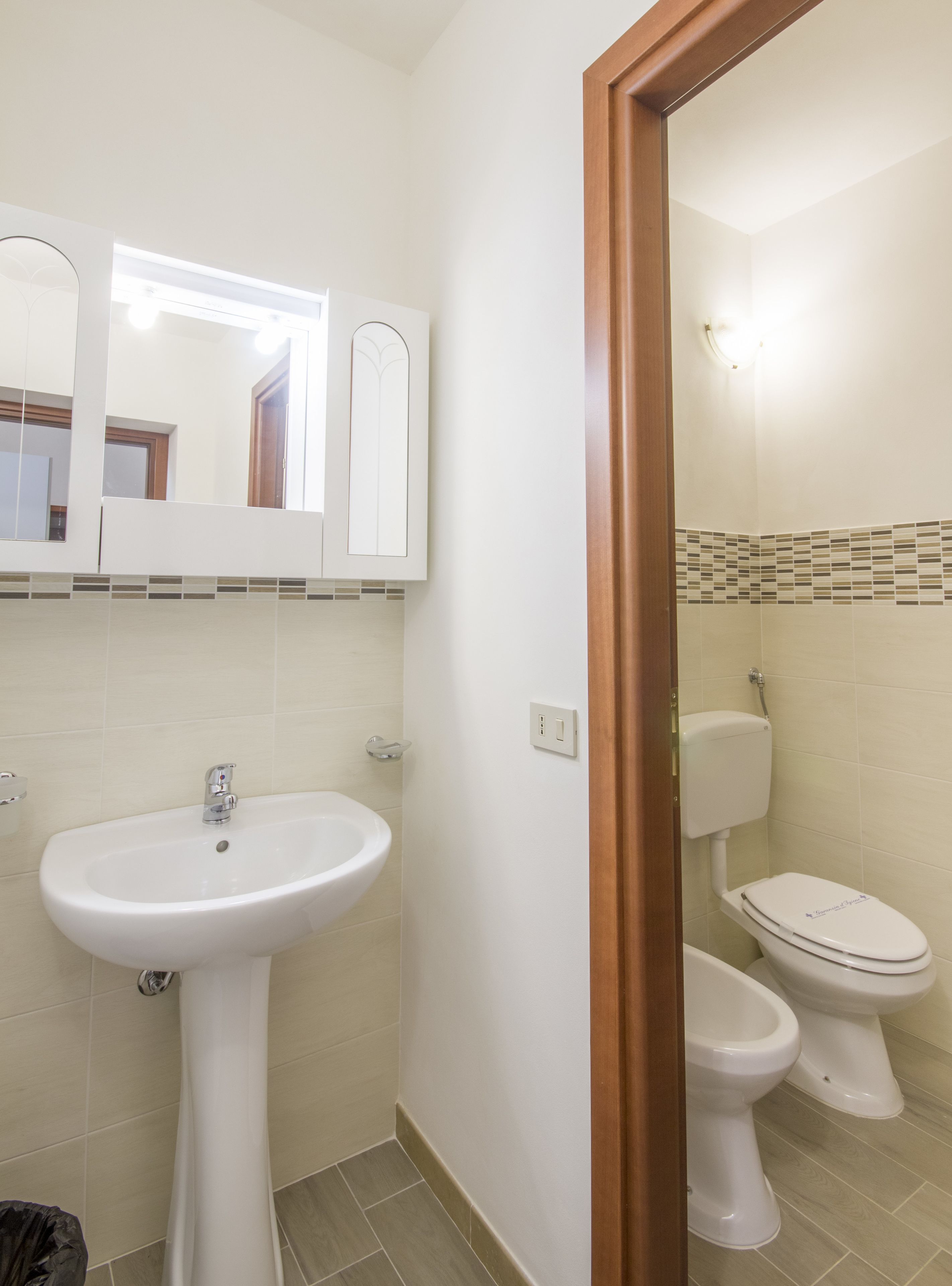 Un baño con un lavamanos blanco, un espejo y dos inodoros.