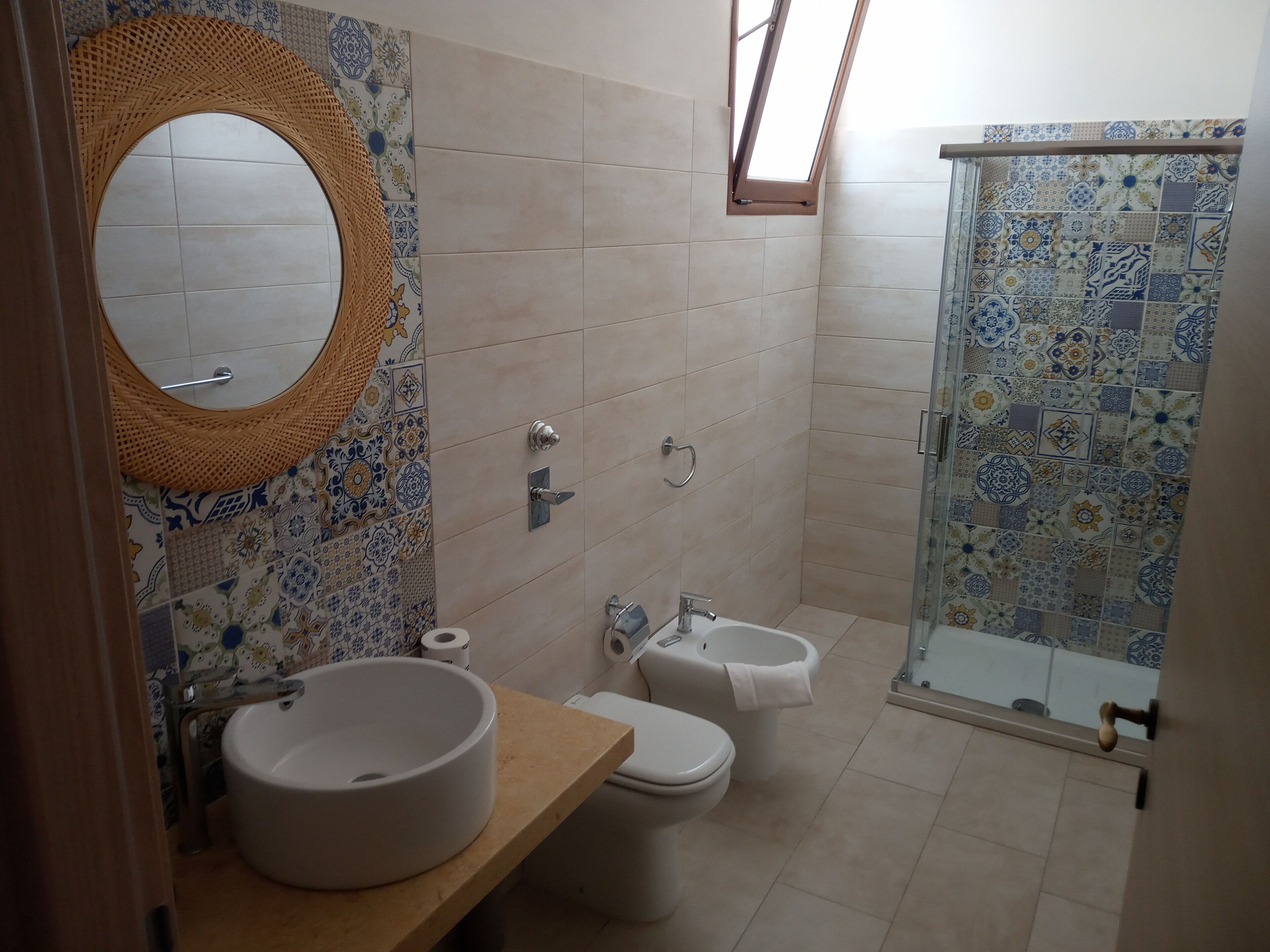 A bathroom with a round mirror, a sink, a toilet, and a shower with patterned tiles.