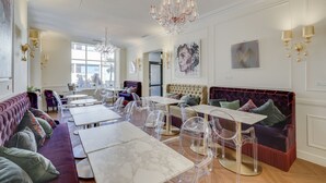 Ein geräumiger Raum mit einer langen Couch, klaren Stühlen und Tischen, einer Kristallleuchtre und Kunstwerken an den Wänden.