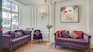 Ein Zimmer mit zwei violetten Sofas, einem kleinen runden Tisch mit einer Vase und einem großen abstrakten Gemälde an der Wand.
