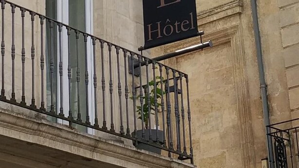 Ein Hotel-Schild mit der Aufschrift "ACANTHE HOTEL" in goldener Schrift auf schwarzem Grund, angebracht an einem Gebäude mit klassizistischer Architektur.