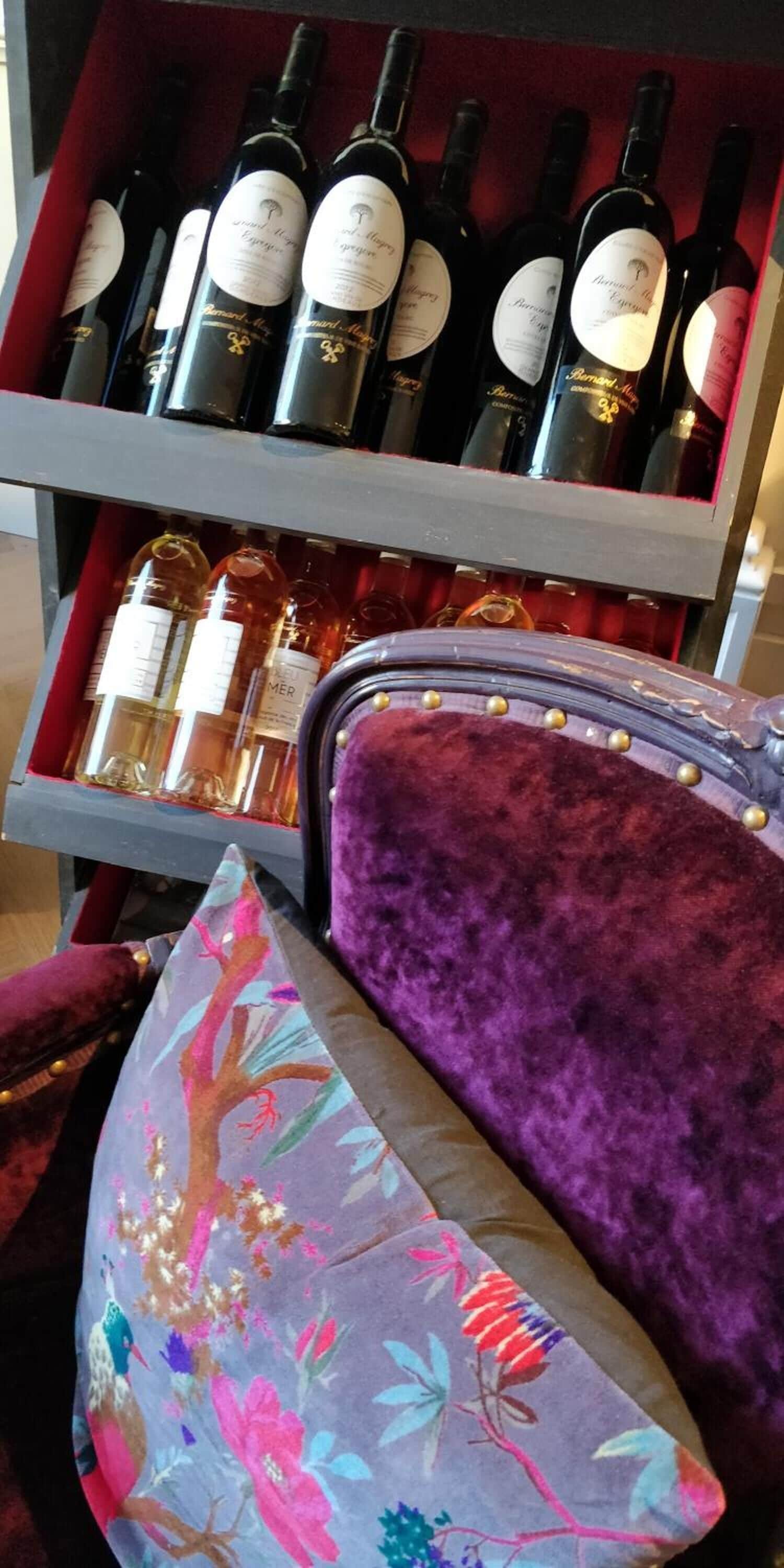 A wine rack with bottles and a velvet chair with a floral pattern.