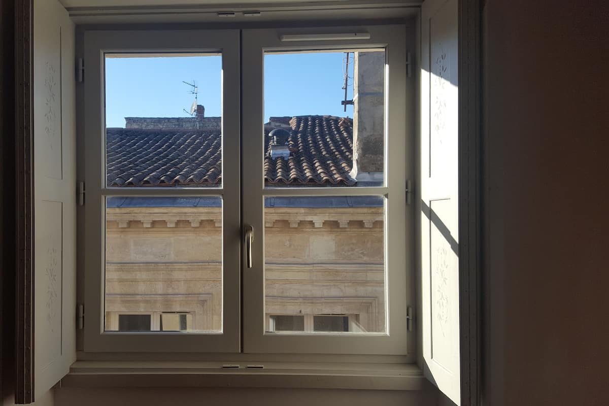 Une fenêtre donnant sur un bâtiment avec un toit en tuiles et une façade en pierre.