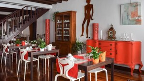 Uma área de refeições com mesas de madeira e cadeiras brancas, um armário vermelho e uma escada.