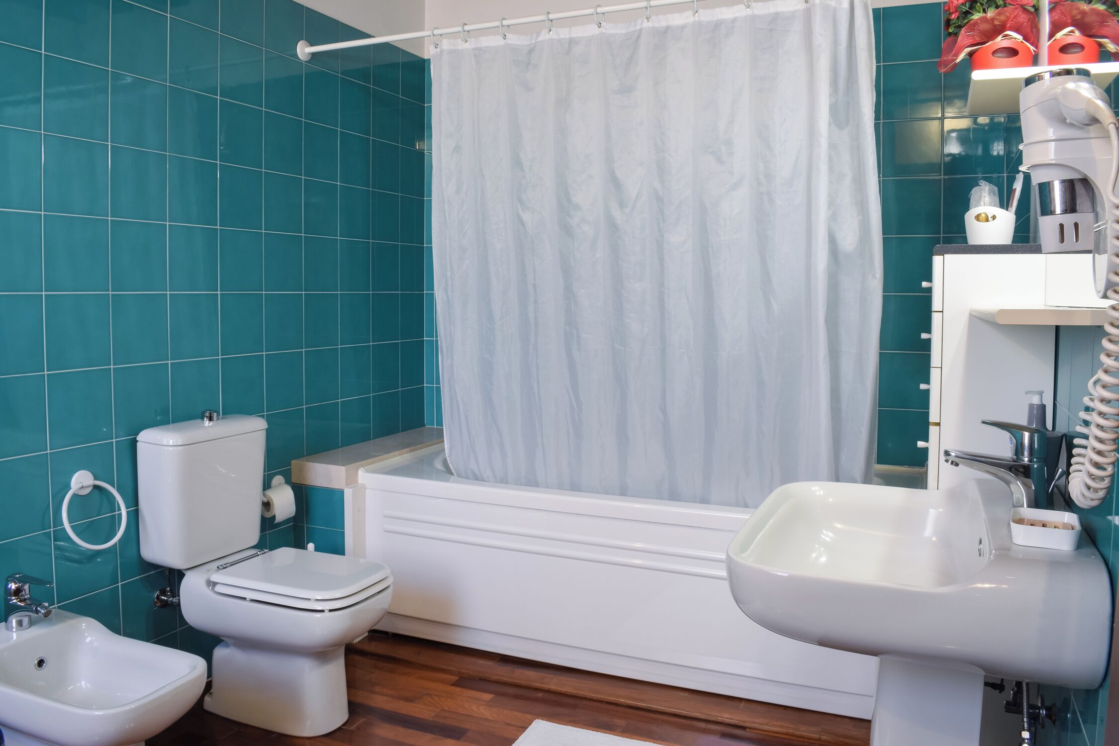 Ein Badezimmer mit türkisblauen Fliesen, einer Badewanne, einer Toilette, einem Bidet und einem Waschbecken.