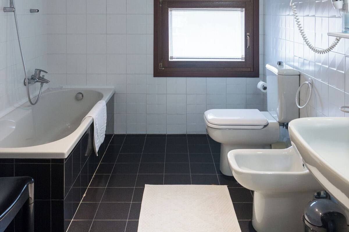 Et moderne badeværelse med badekar, to toiletter og en bidet samt et vindue.