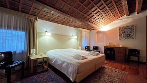 Quarto de hotel com uma cama grande, duas mesas de cabeceira, uma escrivaninha com cadeira, uma pequena mesa com cadeira, uma cafeteira e um tapete.