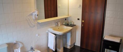 A bathroom with a sink, bidet, and mirror. There is a towel rack and a wooden door.