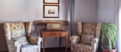 Una sala de estar con dos sillones estampados, una mesita de madera, una radio y una planta en maceta.