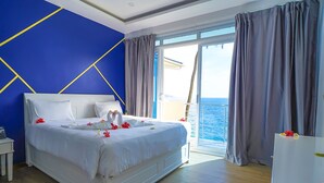 A hotel room with a bed, a nightstand, a view of the sea, and a balcony. -  Itsandra Beach Hotel & Resort (Batsa Itsandra)