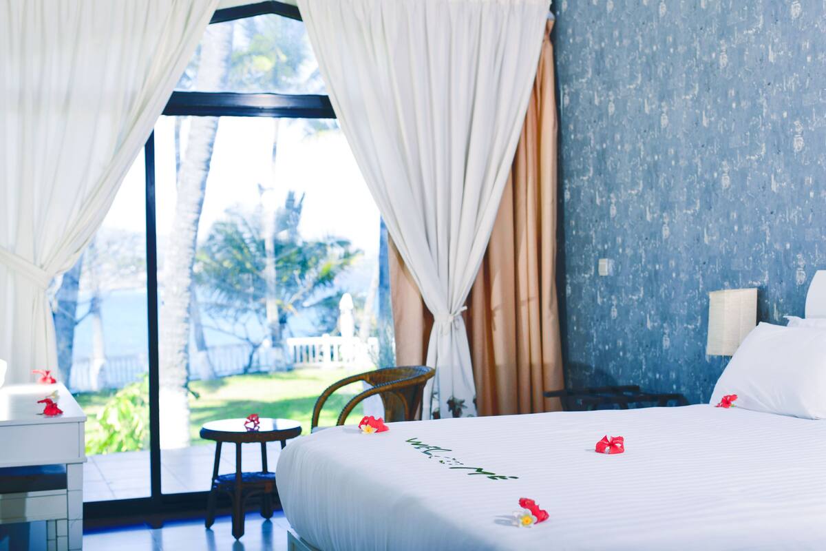 Quarto de hotel com cama, uma cadeira, uma mesinha e vista para o exterior.