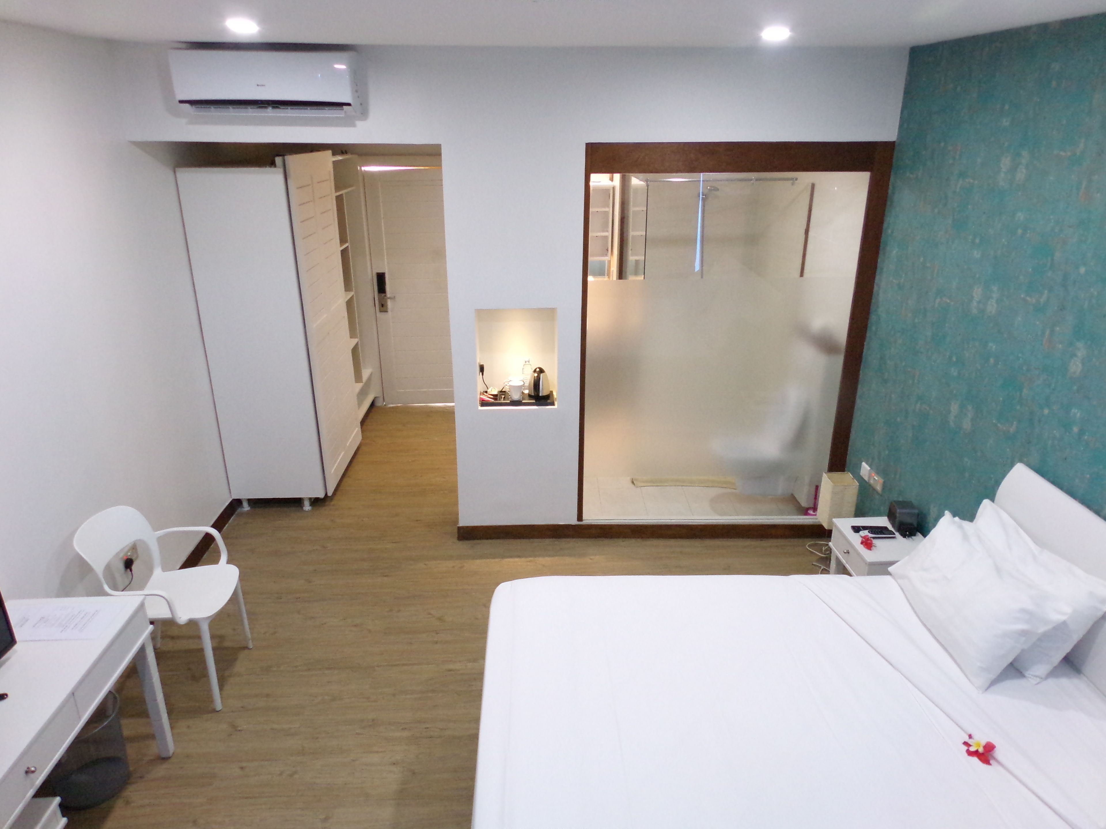 A hotel room with a bed, a desk, a chair, a wardrobe, and a shower area.