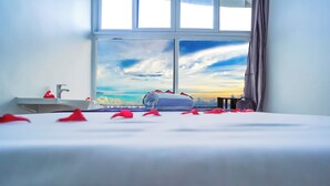 A hotel room with a bed, a window with a view of the sky, a sink, and a towel on the bed. -  Itsandra Beach Hotel & Resort (Batsa Itsandra)
