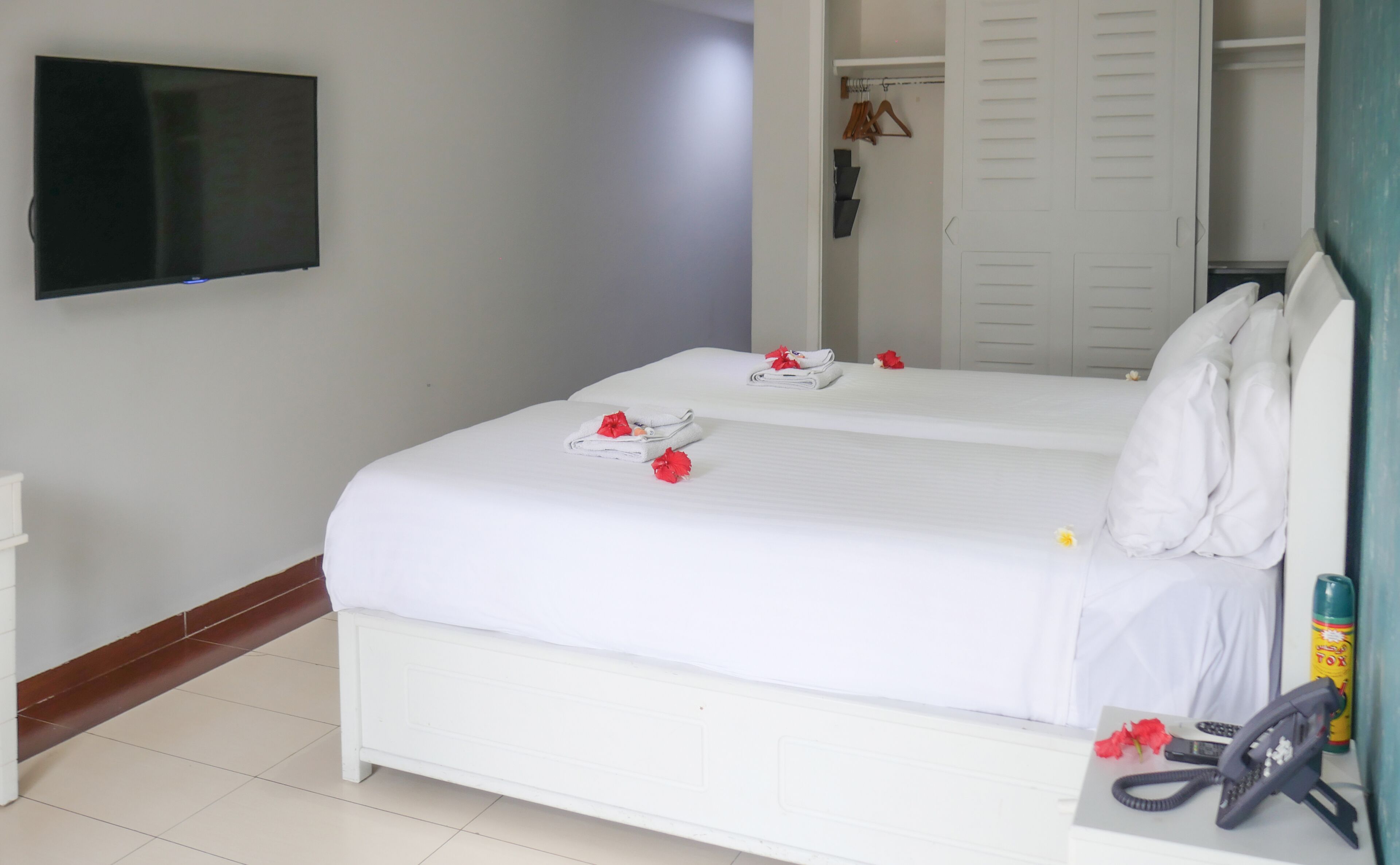 A hotel room with two beds, a TV mounted on the wall, a coat rack, and a bathroom visible through an open door.