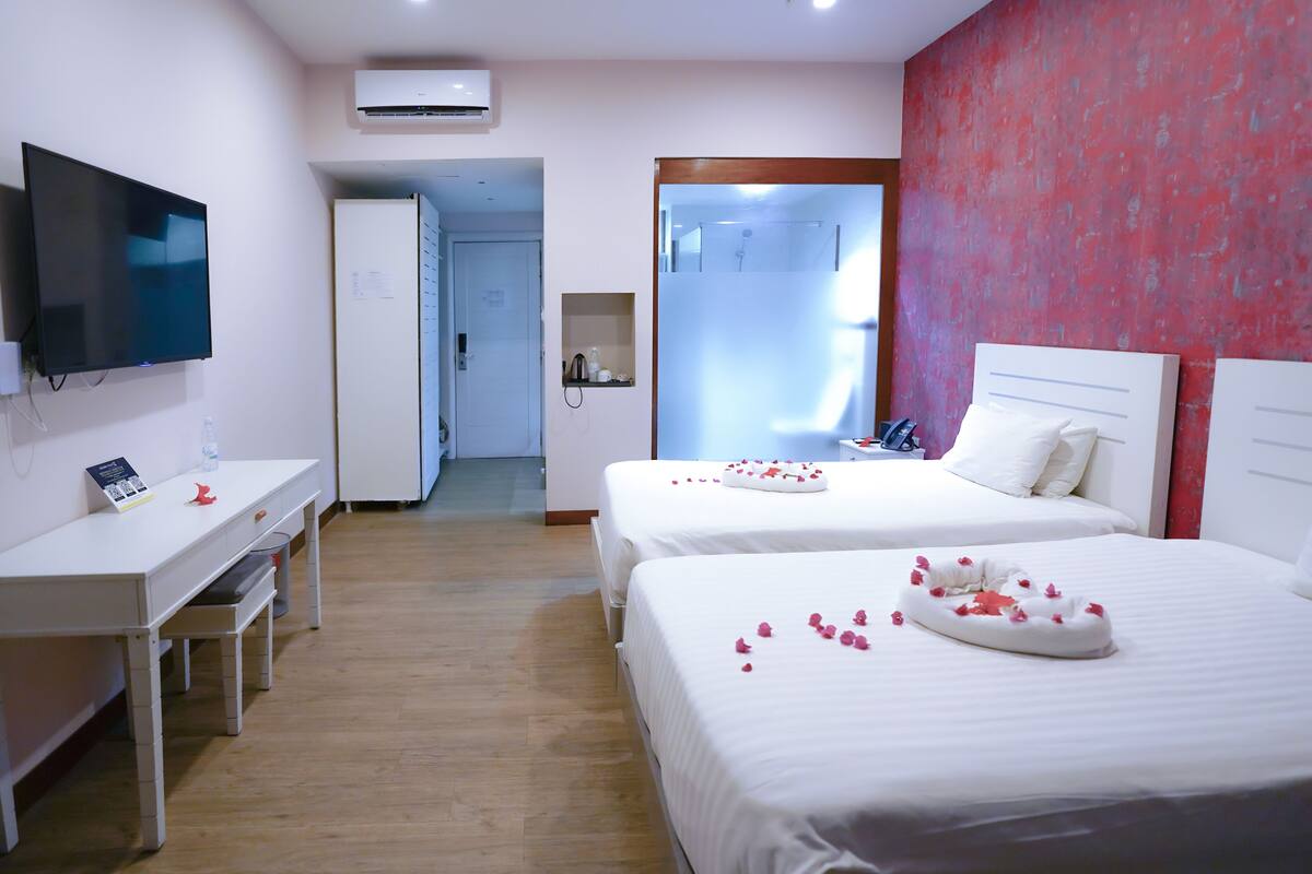 Quarto de hotel com duas camas, uma escrivaninha, televisão e zona de chuveiro.