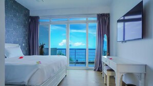 A hotel room with a bed, a desk, a TV, and a large window with a view of the sea. -  Itsandra Beach Hotel & Resort (Batsa Itsandra)