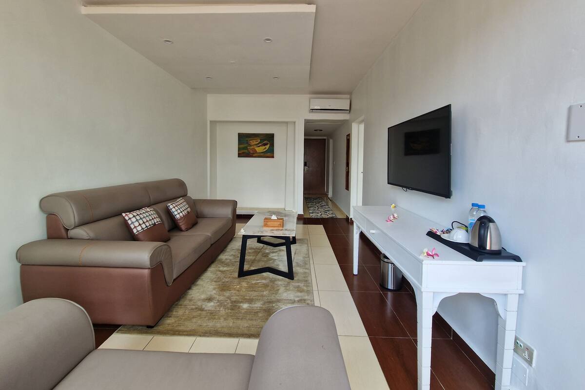 Uma sala de estar moderna com um sofá marrom, uma mesa de centro e uma TV fixada na parede.