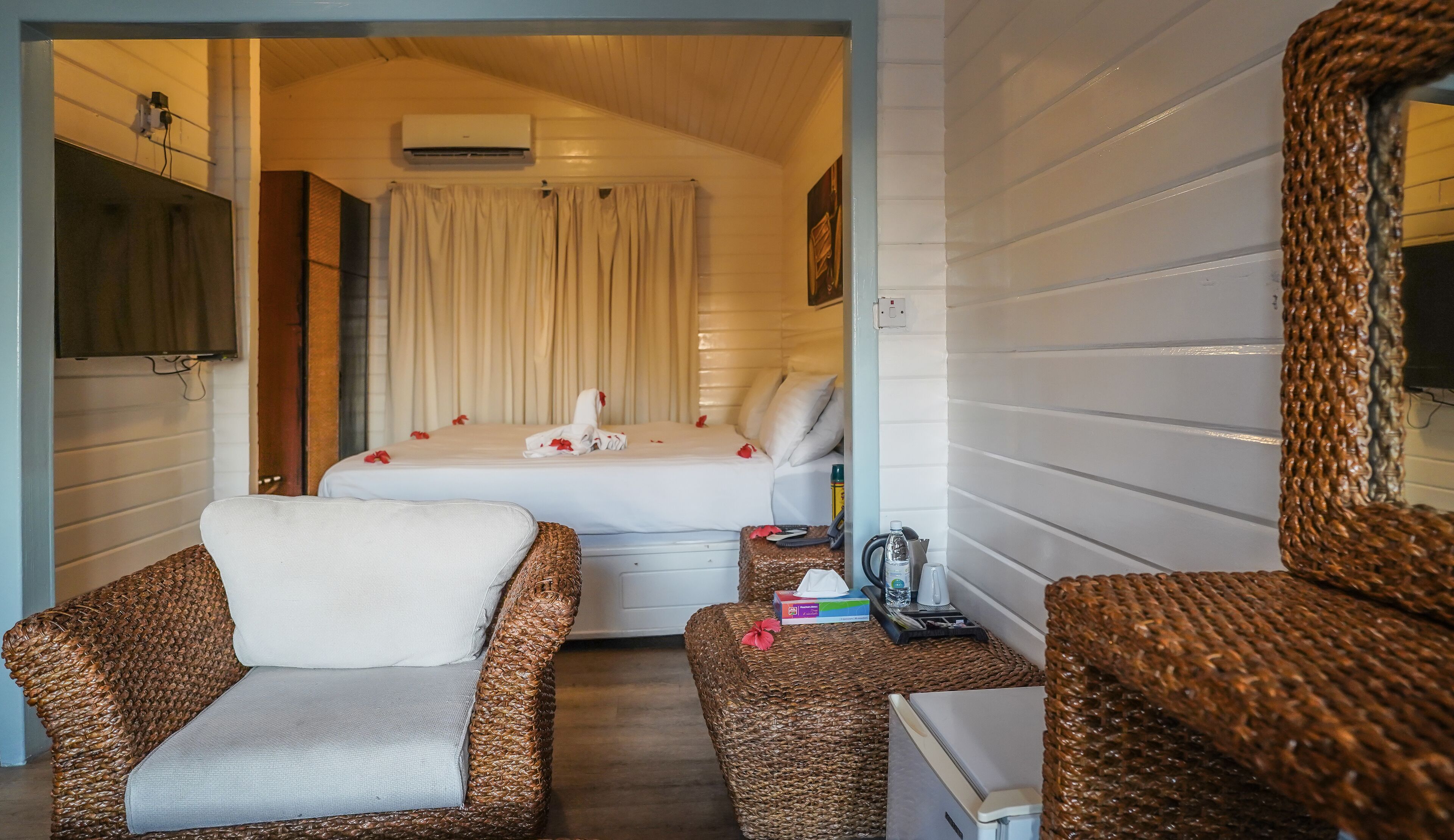 A cozy room with a bed, two wicker chairs, a small table, and a television mounted on the wall.
