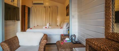 A cozy room with a bed, two wicker chairs, a small table, and a television mounted on the wall.
