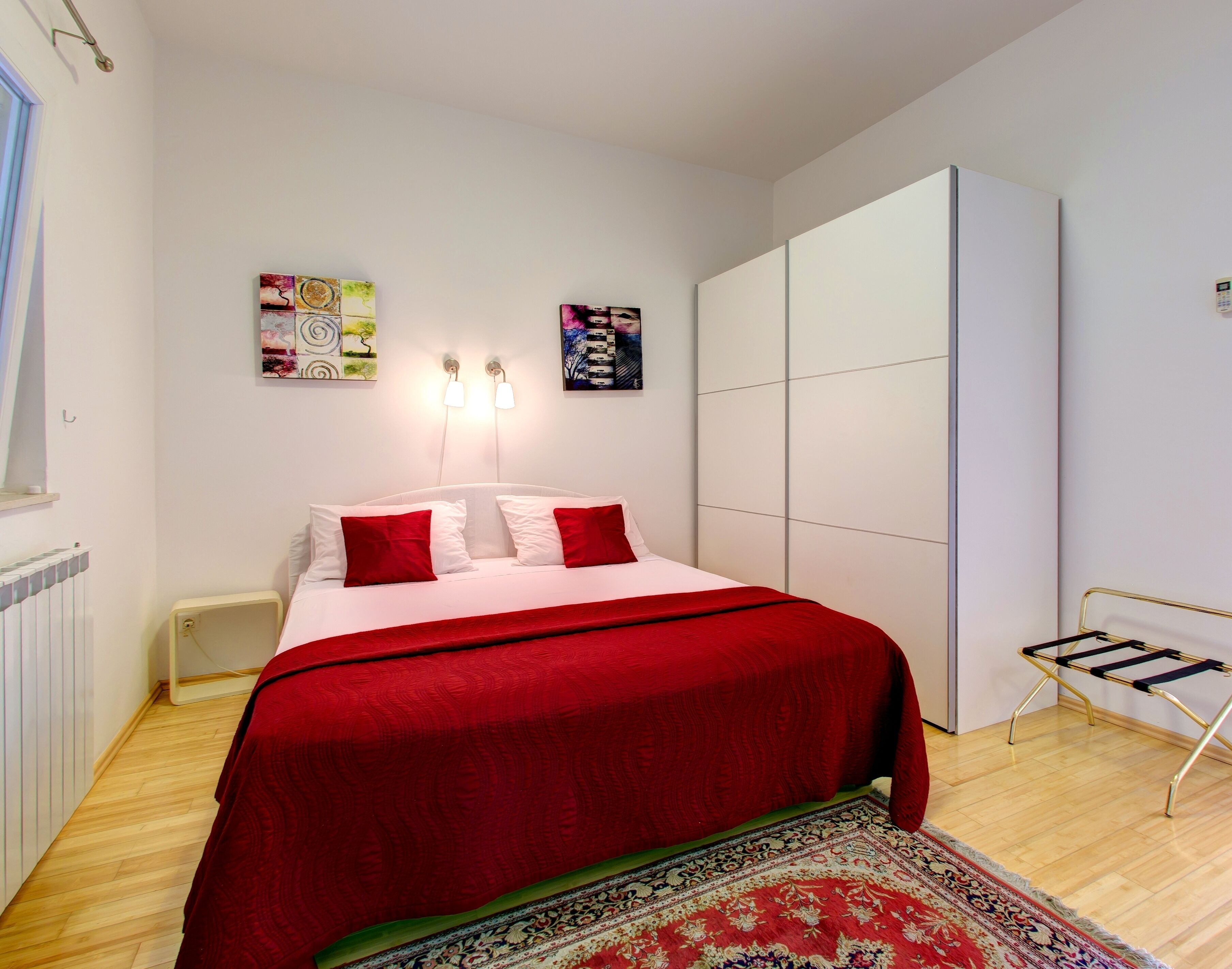 A bedroom with a bed, a radiator, a small bedside table, a wall-mounted light fixture, and a large wardrobe.