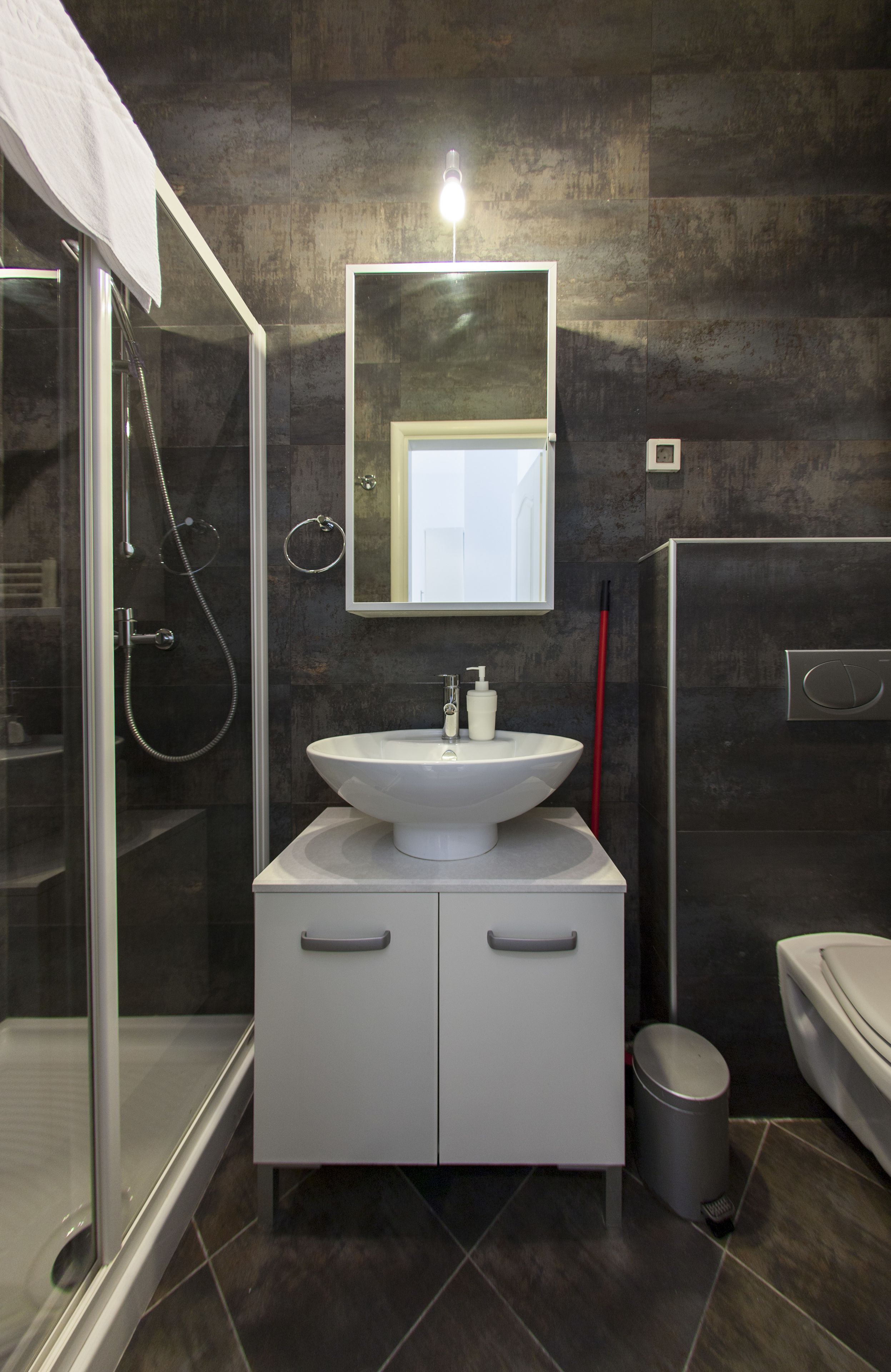 Une salle de bain moderne avec une douche à l’italienne en verre, un lavabo blanc avec un miroir au-dessus et des toilettes sur le côté droit.