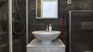 Une salle de bain moderne avec une douche à l’italienne en verre, un lavabo blanc avec un miroir au-dessus et des toilettes sur le côté droit.