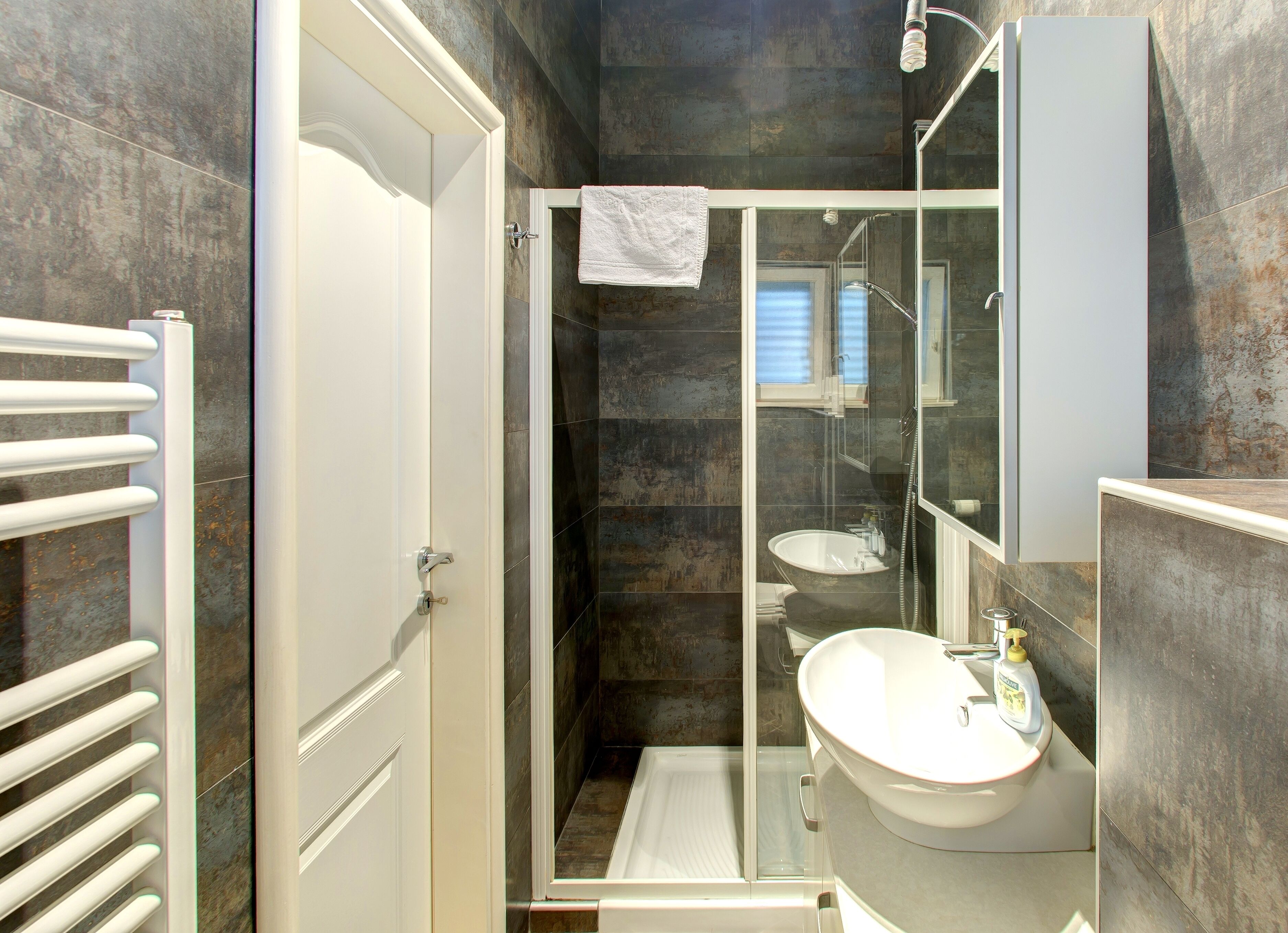 Ein modernes Badezimmer mit einer in Glas eingefassten Dusche, einem weißen Waschbecken und einem Handtuch, das an der Tür hängt.